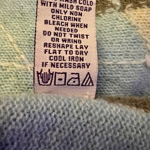 Puede incluir: Una etiqueta de cuidado blanca con texto negro que dice "HAND WASH COLD WITH MILD SOAP ONLY NON CHLORINE BLEACH WHEN NEEDED DO NOT TWIST OR WRING RESHAPE LAY FLAT TO DRY COOL IRON IF NECESSARY". La etiqueta tambi&eacute;n tiene un s&iacute;mbolo en blanco y negro para el lavado a mano.