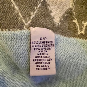 Puede incluir: Una etiqueta blanca con texto negro en un su&eacute;ter azul claro. La etiqueta dice "S/P 80% LAMBSWOOL LAINE D'AGNEAU 20% NYLON/ NYLON MADE IN AUSTRALIA FABRIQUE AUX AUSTRALIE RN 65170 CA 32054".