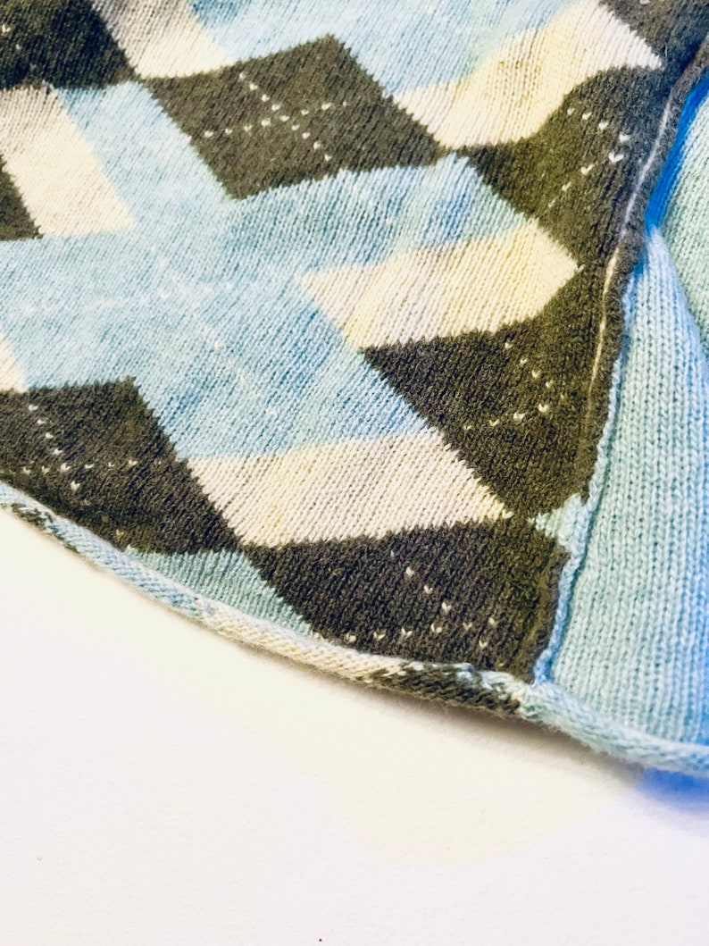 Puede incluir: Primer plano de una tela de punto azul, blanca y marr&oacute;n con un patr&oacute;n de rombos.