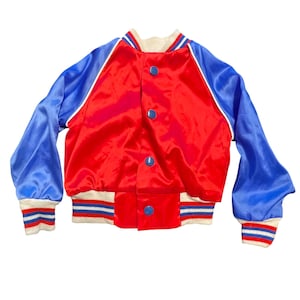 May include: A red satin jacket with blue sleeves and a cream-colored collar and cuffs. The jacket has blue buttons and white trim. The cuffs and waistband have blue and white stripes.