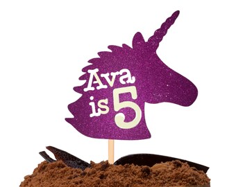 Op de afbeelding: Paarse glitter unicorn cake topper met de tekst "Ava is 5".