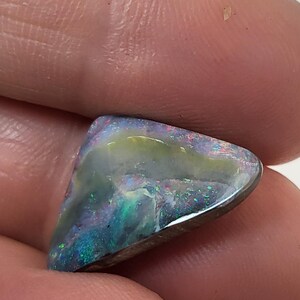 May include: A triangular, iridescent opal gemstone with a dark gray base and flashes of green, blue, and purple.