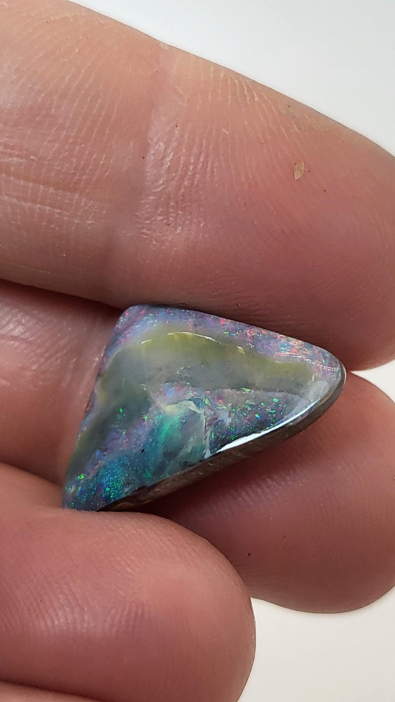 May include: A triangular, iridescent opal gemstone with a dark gray base and flashes of green, blue, and purple.