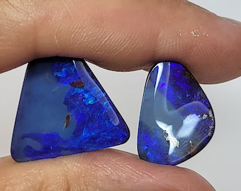 May include: Two blue opal gemstones, one triangular and one teardrop shaped, are held in a hand.