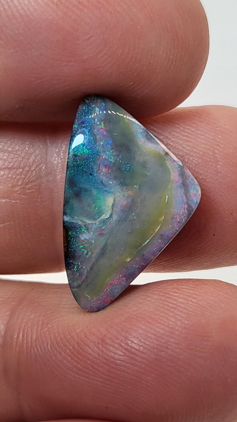 May include: A triangular, iridescent opal gemstone with a blue, green, and white color pattern. The opal is set in a silver ring.