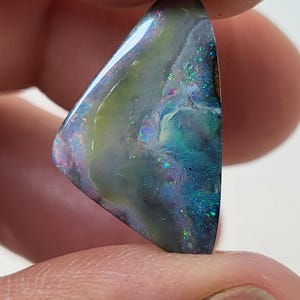 May include: A triangular piece of opal with a dark blue, green, and purple iridescent sheen. The opal has a light green and white pattern.