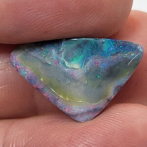 May include: A triangular shaped opal gemstone with a blue, green, and purple iridescent sheen. The opal has a white and yellow base color.