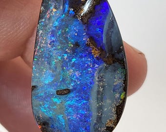 May include: A teardrop-shaped blue opal gemstone with a black matrix and iridescent flashes of color.