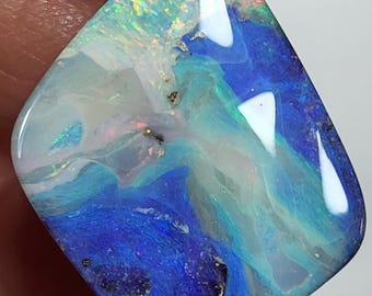 May include: A polished, iridescent opal gemstone with a captivating display of colors. The stone features swirling patterns of blue, white, green, and hints of gold. The opal is held between fingers, showcasing its unique, natural beauty.