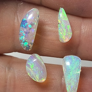 May include: Four iridescent opal gemstones in various shapes and sizes. The opals have a white base with green and blue flashes.