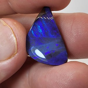 Könnte beinhalten: Ein dunkelblauer und violetter Opal-Cabochon in Tropfenform. Der Opal ist in einer silbernen Fassung gefasst und hat einen hohen Glanz.