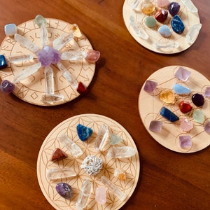 May include: Three wooden circular trays with geometric designs and various crystals in different colors, including clear, purple, pink, red, blue, green, and yellow.