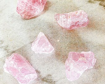 May include: Five pink rose quartz crystals of varying sizes and shapes on a light gray background.