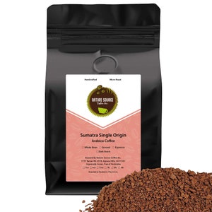 May include: A black bag of Sumatra Single Origin Arabica coffee from Nature Source Coffee Inc. The bag is labeled with the company's logo, the coffee's origin, and the roast type. The bag is sitting on a pile of ground coffee.