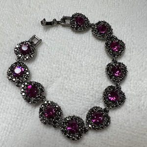 May include: A black bracelet with a silver clasp and purple rhinestones. The bracelet has a total of 10 rhinestones, each set in a circular frame.