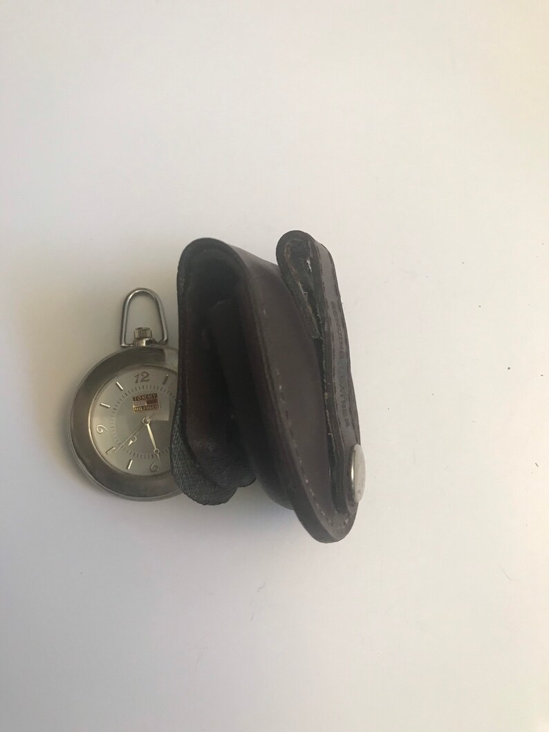 May include: A silver pocket watch with a white face and black hands. The watch is in a brown leather case with a silver button.