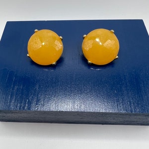May include: A pair of round, yellow, glass earrings with gold metal settings.