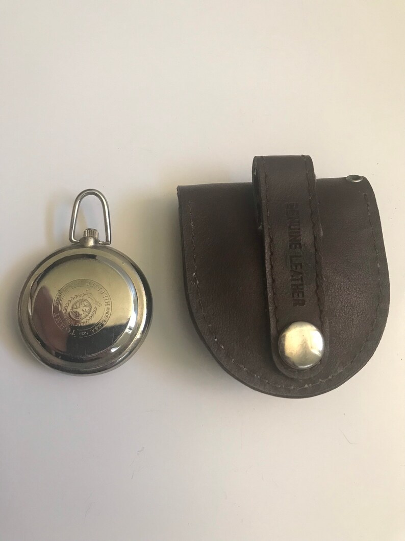 May include: A silver pocket watch with a black face and a leather carrying case. The case has the words "Genuine Leather" embossed on it.