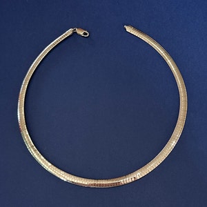 Peut inclure: Un collier en chaîne argenté au design simple et élégant. La chaîne est composée de petits maillons plats étroitement entrelacés.