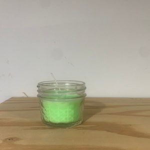 May include: A green candle in a clear glass jar with a white wick.