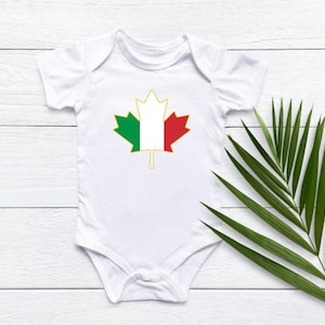 May include: White baby onesie with a green, white, and red maple leaf design. The leaf is outlined in gold.