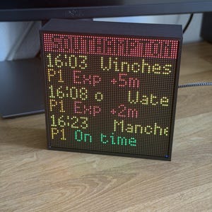 May include: A square black digital display board featuring a dot matrix screen that shows train schedule information. The text reads SOUTHAMPTON, 16:03 Winches P1 Exp +5m, 16:08 o Wate P1 Exp +2m, and 16:23 Manche P1 On time in red, yellow, and green.