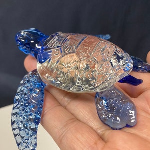May include: A blue glass sea turtle figurine with a detailed, patterned shell. The turtle's head and flippers are also blue and have a textured surface.