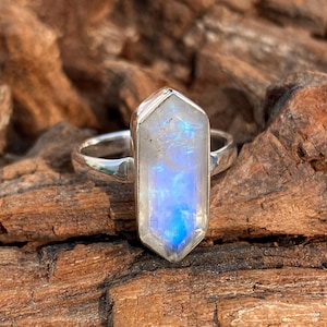 Puede incluir: Un anillo de plata con una gran piedra de luna iridiscente engastada en una forma hexagonal facetada.
