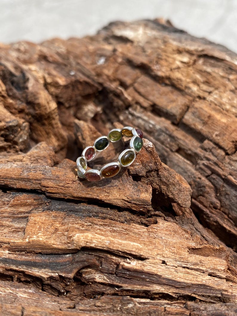 May include: A silver ring with a band of oval-shaped gemstones in shades of green, brown, and pink.