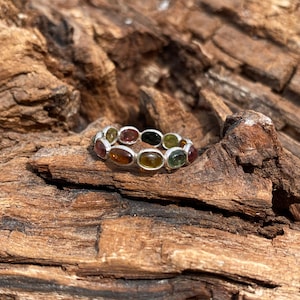 May include: A silver ring with a band of oval-shaped gemstones in shades of green, brown, and orange.