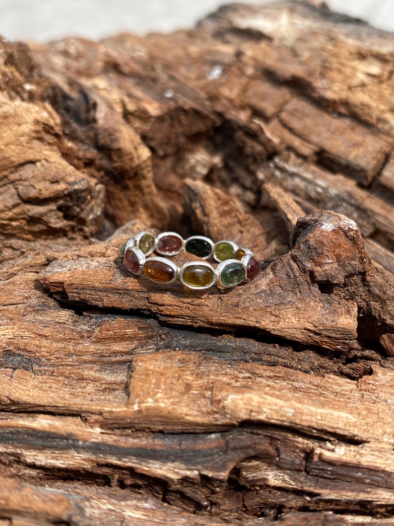 May include: A silver ring with a band of oval-shaped gemstones in shades of green, brown, and orange.