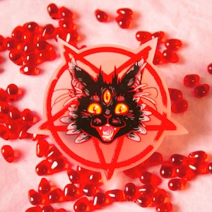 Puede incluir: Un gato negro con tres ojos y una sonrisa amenazante se representa dentro de un pentagrama rojo. La imagen está sobre un fondo blanco.