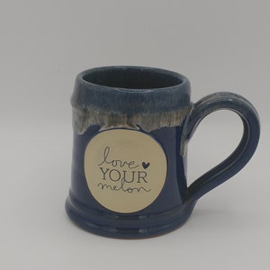 May include: A blue ceramic mug with a white glaze and a gold sticker that says "love your melon" with a small heart.