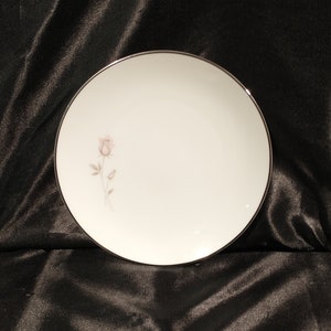 May include: A white ceramic plate with a silver rim and a single pink rose design.