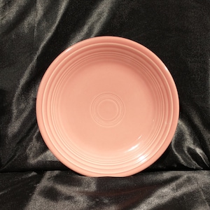 May include: A pink ceramic dinner plate with a slightly raised rim and concentric circles in the design.
