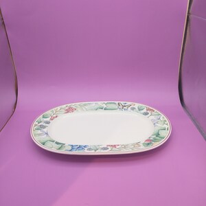 May include: White oval serving platter with a floral border featuring green leaves, red berries, blue grapes, and a butterfly. The border is outlined in red.