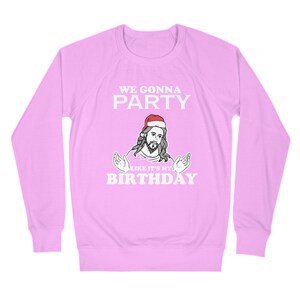 May include: A pink long-sleeved sweatshirt with a white graphic of Jesus wearing a Santa hat and the text "We gonna party like it's my birthday".