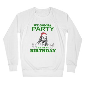 May include: White long-sleeve sweatshirt with green text that reads "We gonna party like it's my birthday". A cartoon image of Jesus wearing a Santa hat is in the center of the text.