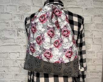 Könnte beinhalten: Eine graue Kordeltasche mit Totenkopf- und Blumenmuster. Die Tasche hat eine weiße Kordel und einen grauen Totenkopf-Druck auf der unteren Hälfte.