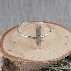 Puede incluir: Un anillo de barra martillado de plata sobre una base de madera. El anillo es simple y minimalista.