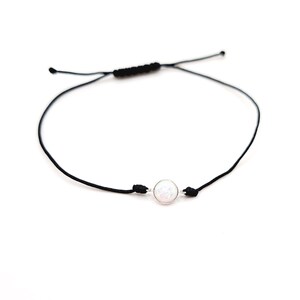 Puede incluir: Un brazalete simple de cuerda negra con una cuenta de ópalo blanco.