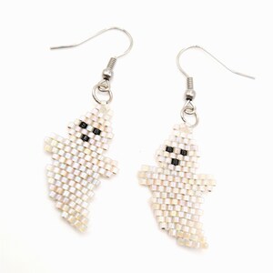 May include: A pair of handmade ghost earrings. Each earring is crafted from iridescent white beads, forming a ghost shape with black bead eyes and mouth. The earrings hang from silver-colored fish hook ear wires.