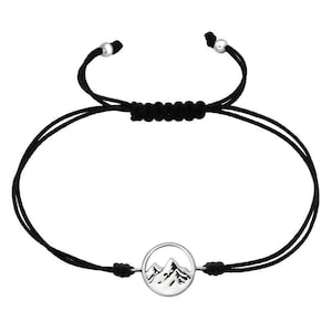 May include: A black string bracelet with a silver charm featuring a mountain silhouette. The charm is round and has a smooth, polished finish.