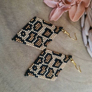Op de afbeelding: Een paar gouden, zwarte en beige kralen oorbellen met een geometrische diamantvorm. De oorbellen hebben een luipaardprint.