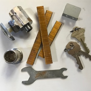 May include: A collection of assorted hardware items including a silver wrench, a silver valve, a silver cap, three gold-colored metal strips, a silver metal plate with two holes, and two silver keys with key rings.