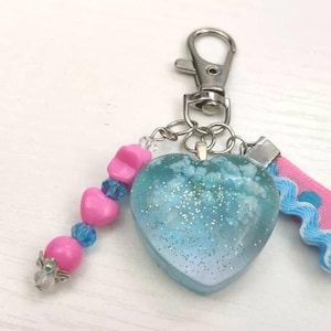 May include: A blue glitter heart charm with pink and blue beads and a pink and blue ribbon attached to a silver key chain.
