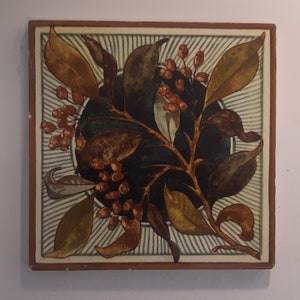 May include: A square ceramic tile with a decorative floral design. The tile features a stylized branch with leaves in shades of brown, green, and gold. The branch is adorned with clusters of small red berries. The tile has a white background with a blue and white striped pattern.