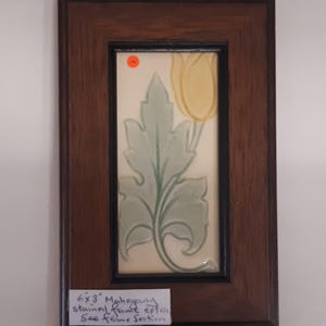 May include: A framed ceramic tile featuring a green and yellow floral design. The tile is framed in a dark wood frame. The label reads "6x3" Mahogany stain/paint extra See frame section"