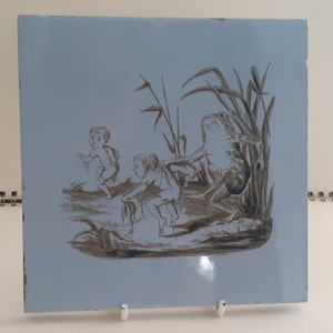 Peut inclure: Un carreau de céramique bleu et blanc avec une illustration en noir et blanc de deux enfants et une grenouille dans un marais.