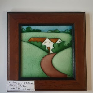 Puede incluir: Un azulejo de cerámica enmarcado con una pintura de un camino sinuoso que conduce a dos casas en un campo verde. El marco tiene 15,24 cm de ancho y está hecho de madera teñida de caoba. El texto de la etiqueta dice "6" Mahogany Stained Frame Extra See Frame Section"